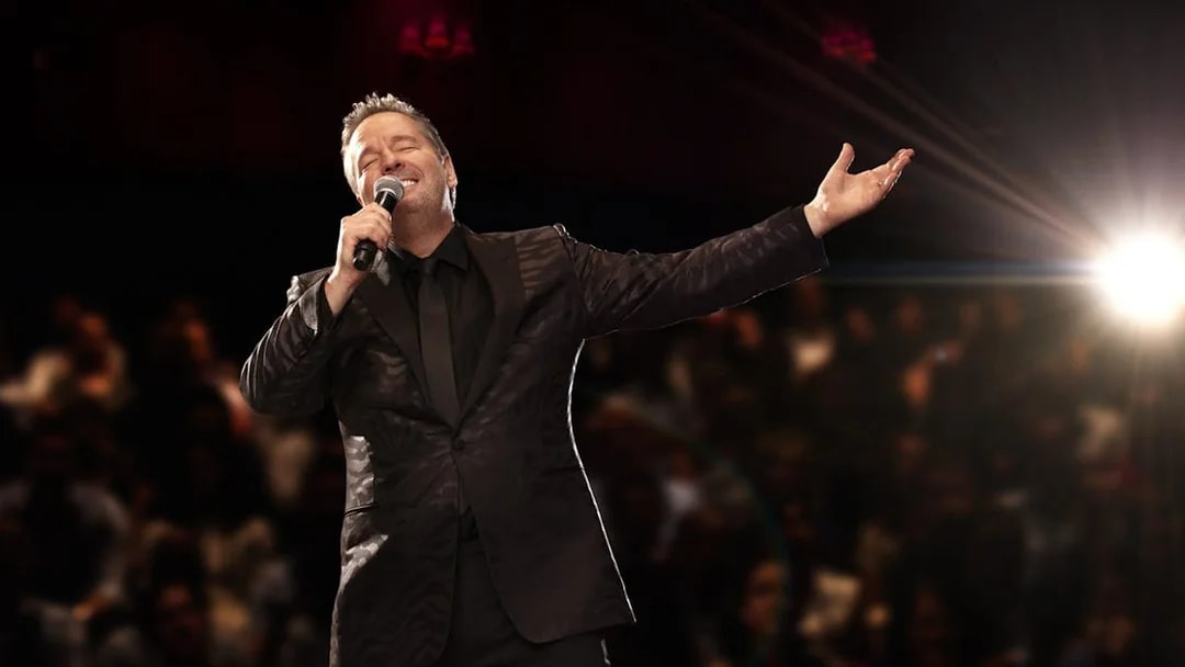 Entertainer performing on stage with microphone, spotlight, and audience in background.