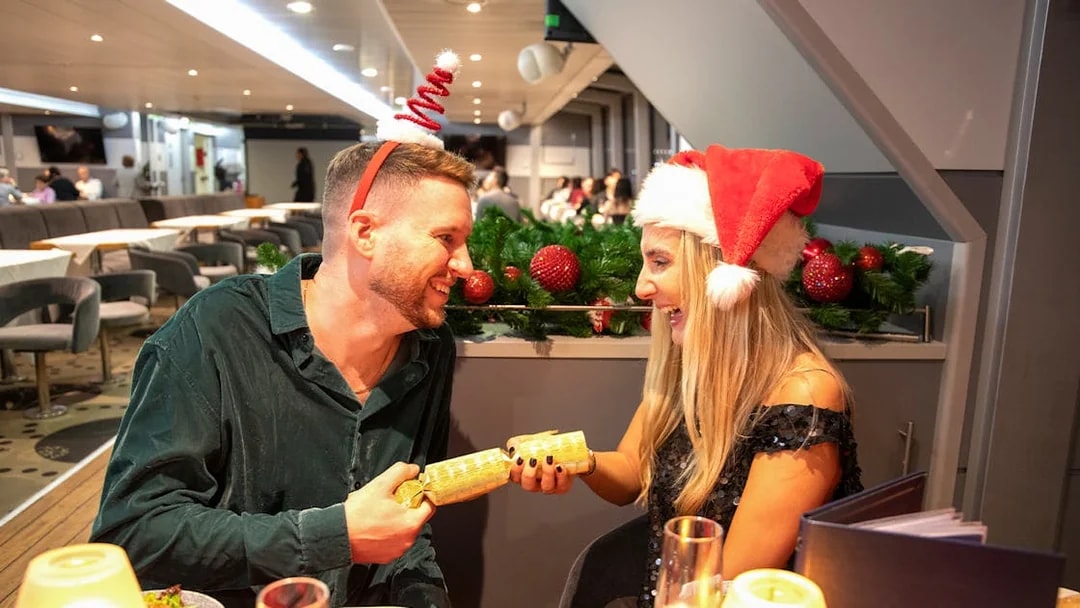 Guests enjoying Christmas dinner on Thames River cruise with festive hats.