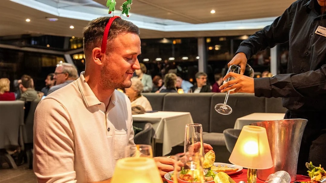 Guests enjoying Christmas dinner on Thames River cruise with festive decorations.