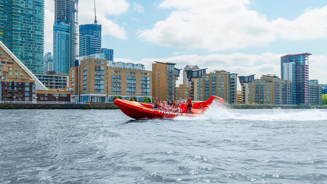Thames speed boat with passengers cruising past London riverside buildings.