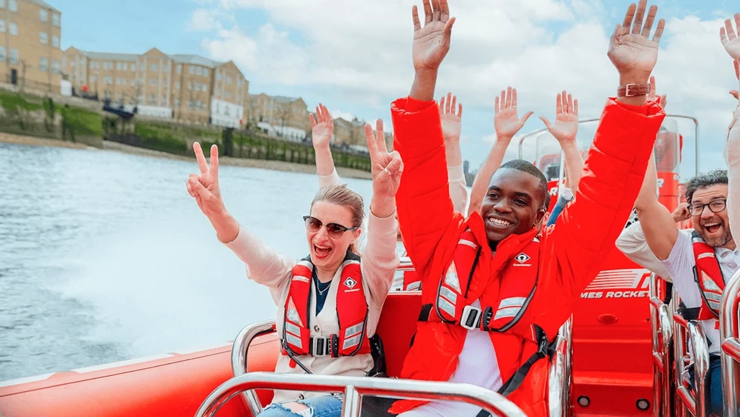 People enjoying a Thames speed boat ride in London, raising hands and smiling.