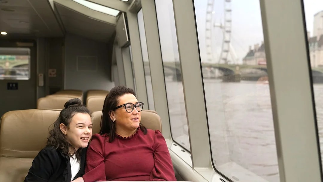 Passengers enjoying Thames River Uber Boat with London Eye view.