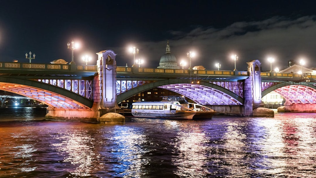 Uber Boat on Thames River at night passing under illuminated London bridge.