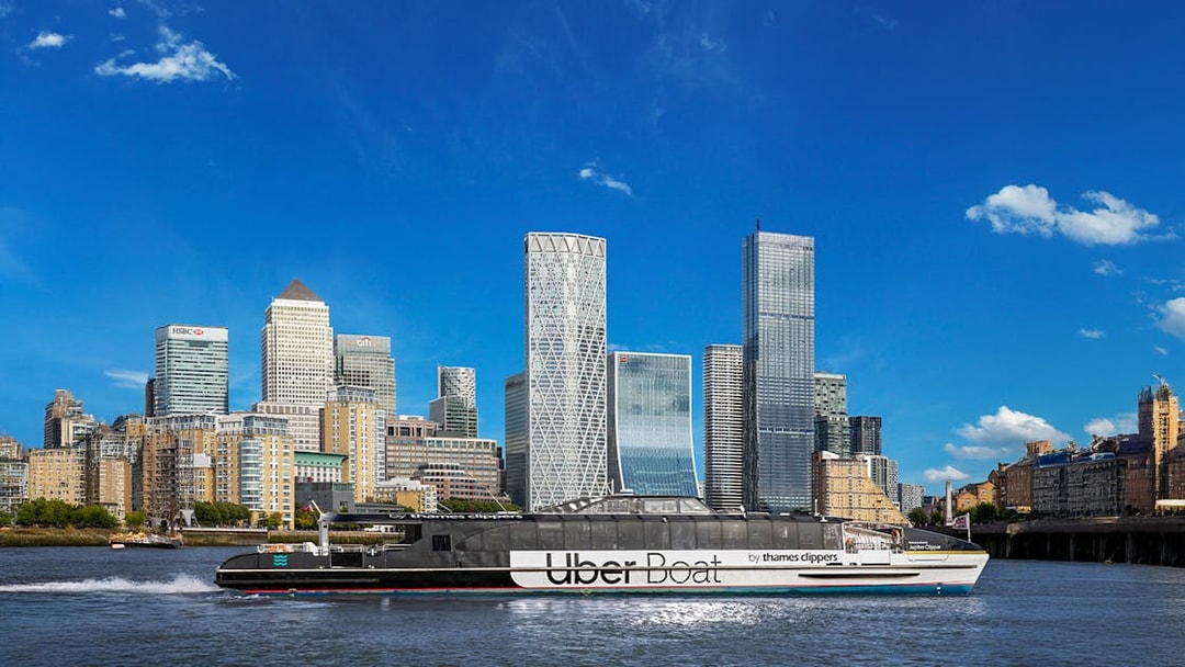 Uber Boat on Thames River passing Canary Wharf skyscrapers.