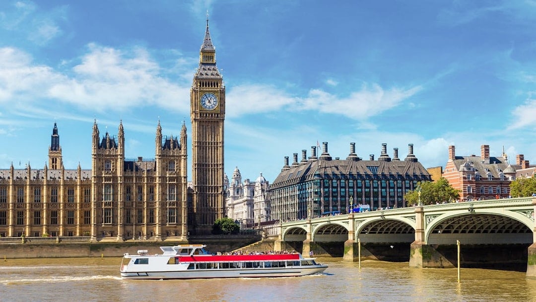 Westminster cruise boat on the Thames with Big Ben and bridge in view.