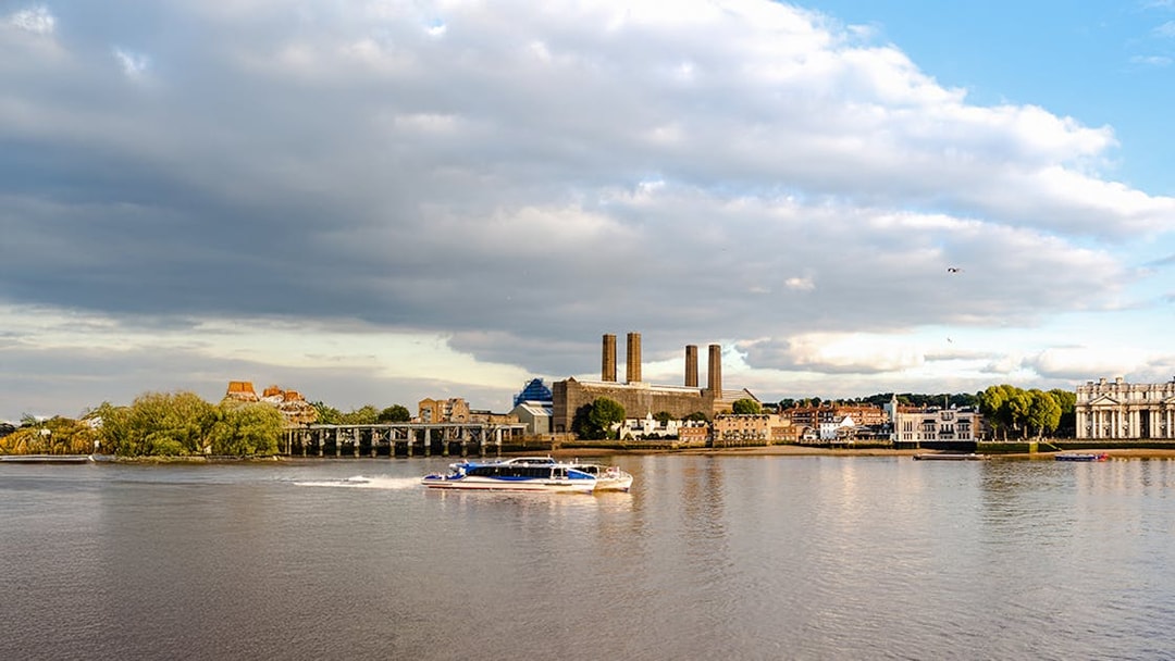 Thames River ferry passing Greenwich riverfront buildings in London.