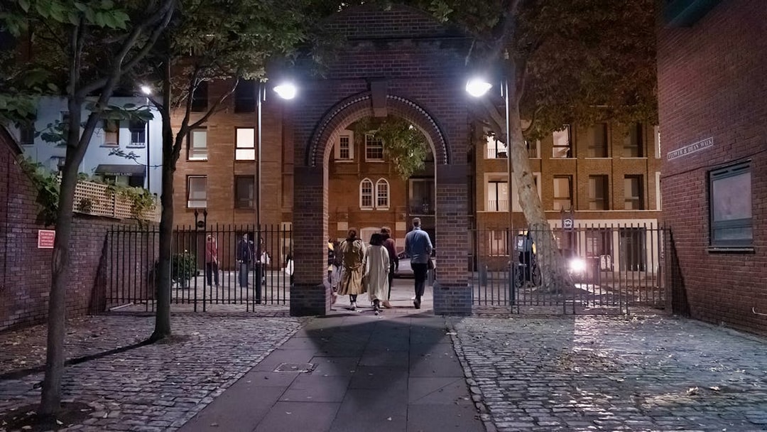 Group walking through a brick archway on a Jack the Ripper tour in London at night.
