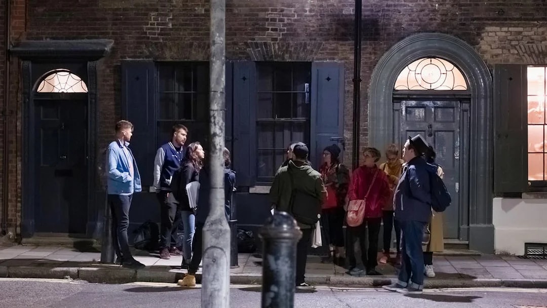 Group of people on a Jack the Ripper tour standing outside historic London building at night.