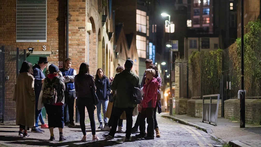 Group of people on a nighttime Jack the Ripper tour in a historic London alley.
