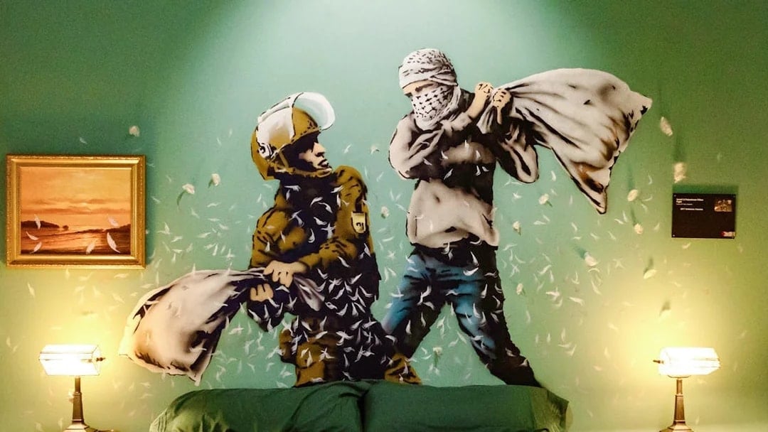 Street art mural of a pillow fight in the Banksy Museum room, featuring a soldier and a masked figure.