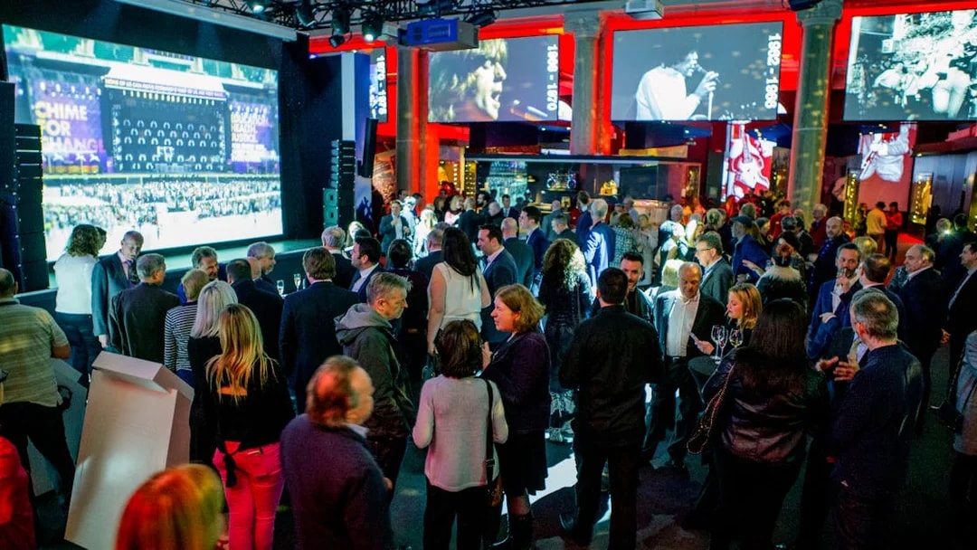 Crowd at The British Music Experience with concert footage on screens.