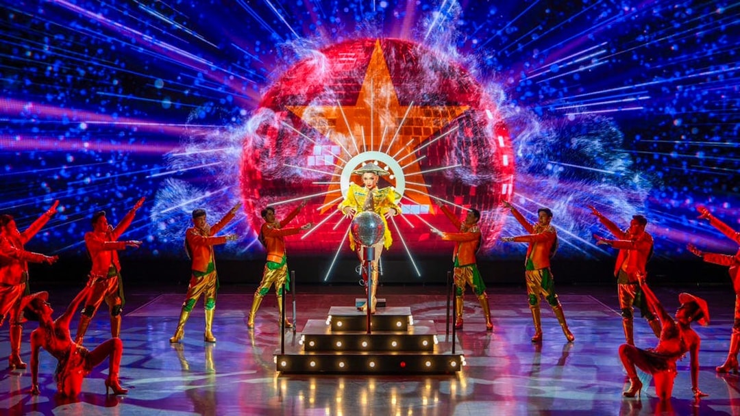 Performers in vibrant costumes on stage with colorful lights at a Colosseum show.