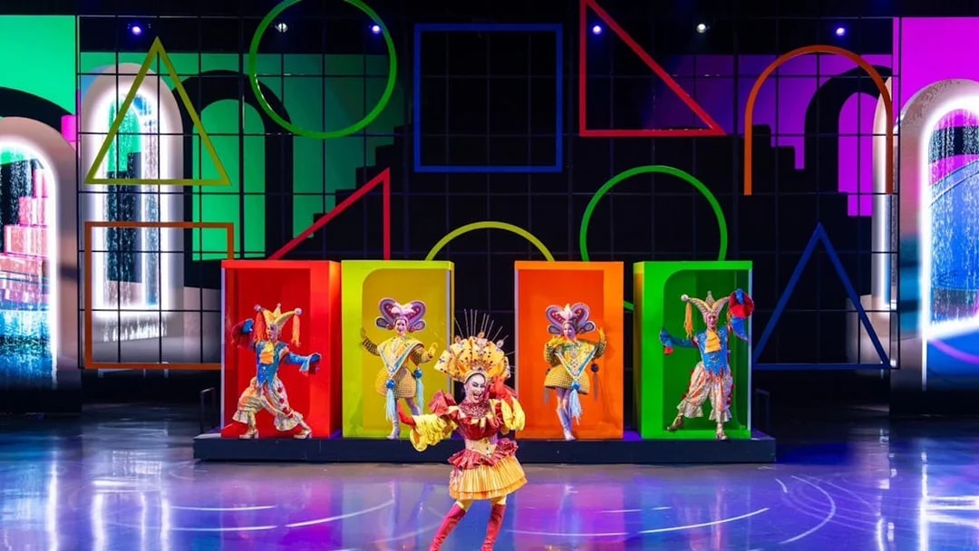 Performers in colorful costumes on stage at a vibrant Colosseum show.