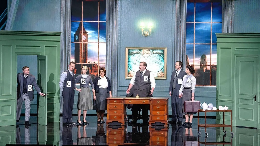 Actors on stage in a comedic spy play set in London with Big Ben visible through the window.