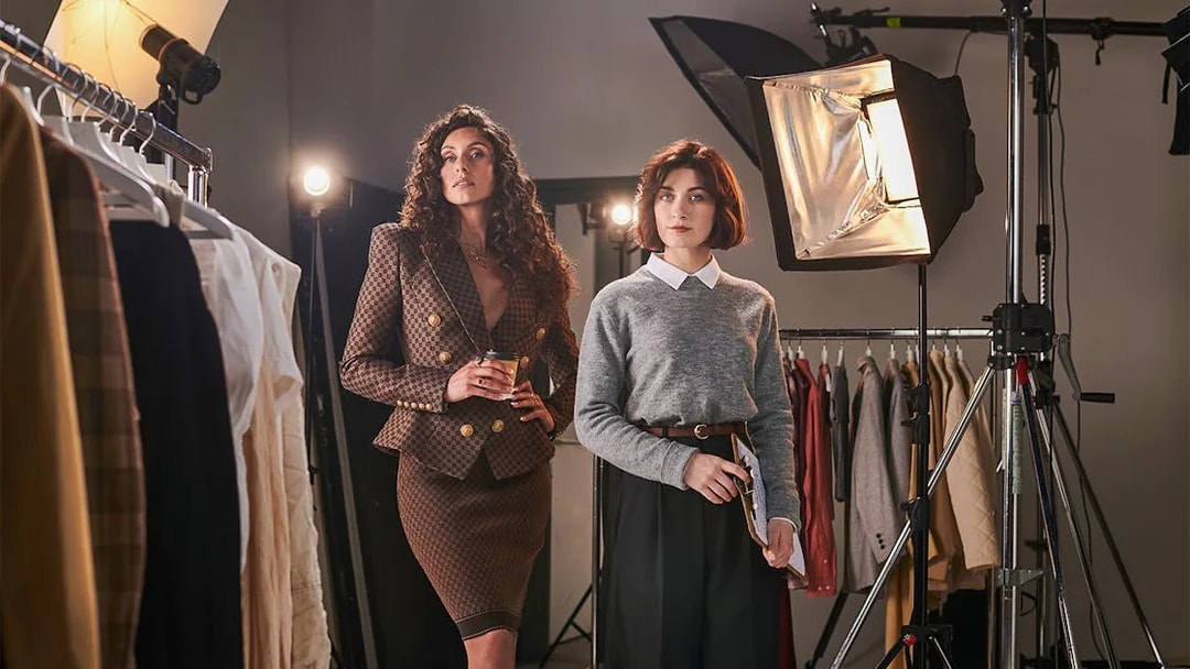Fashion studio setup with two women among clothing racks and studio lights.