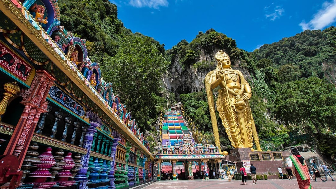 Batu Caves entrance with colorful steps and large golden statue, Kuala Lumpur.