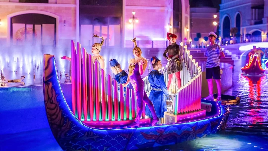 Performers in colorful costumes on a lit boat during The Land of Legends boat parade.