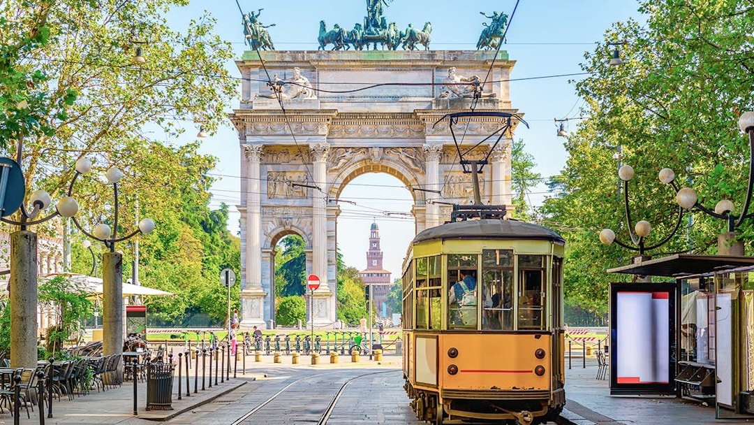 Milan vintage tram passing by Arco della Pace in a tree-lined street.