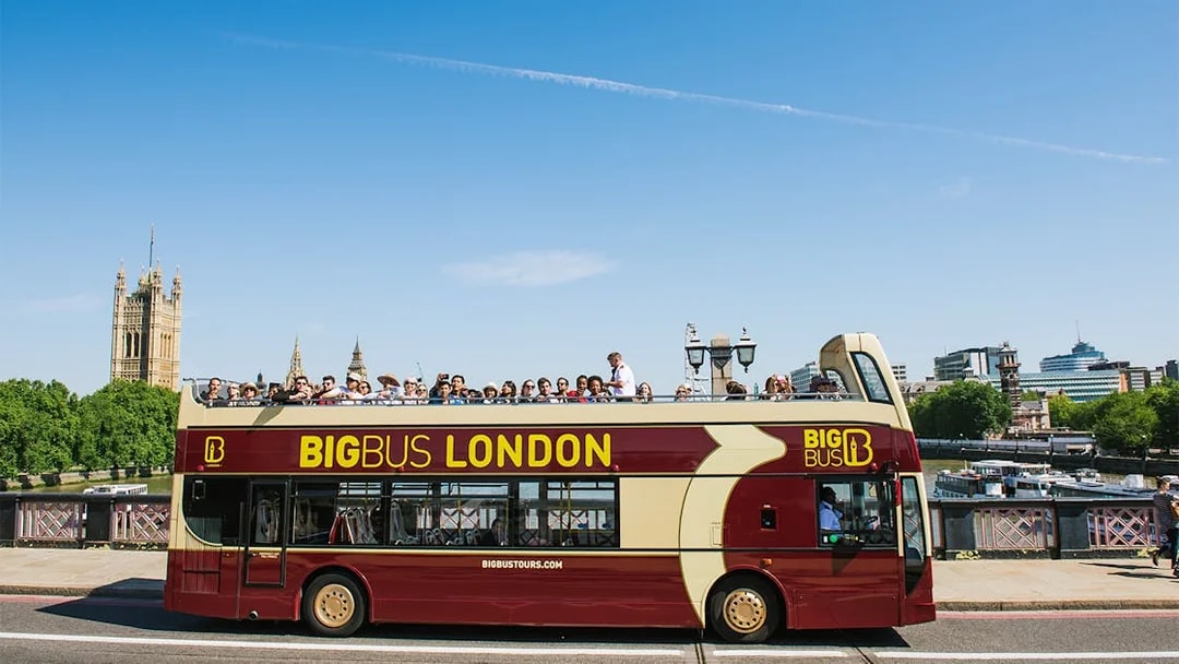 Big Bus tour in London with passengers, passing by the Houses of Parliament.