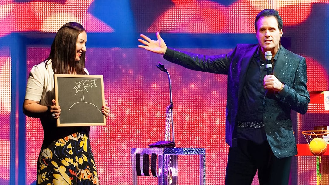 Performer on stage with a participant holding a drawing during The Mentalist show.