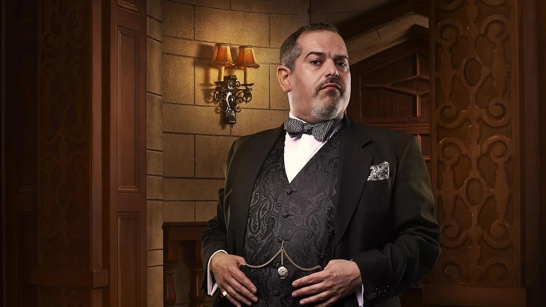 Man in formal attire standing in a vintage theater setting for The Mousetrap.