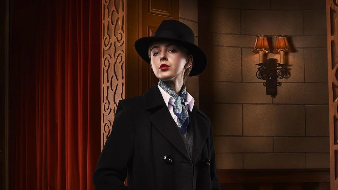 Person in vintage attire with hat and scarf, standing in a theater setting for The Mousetrap.