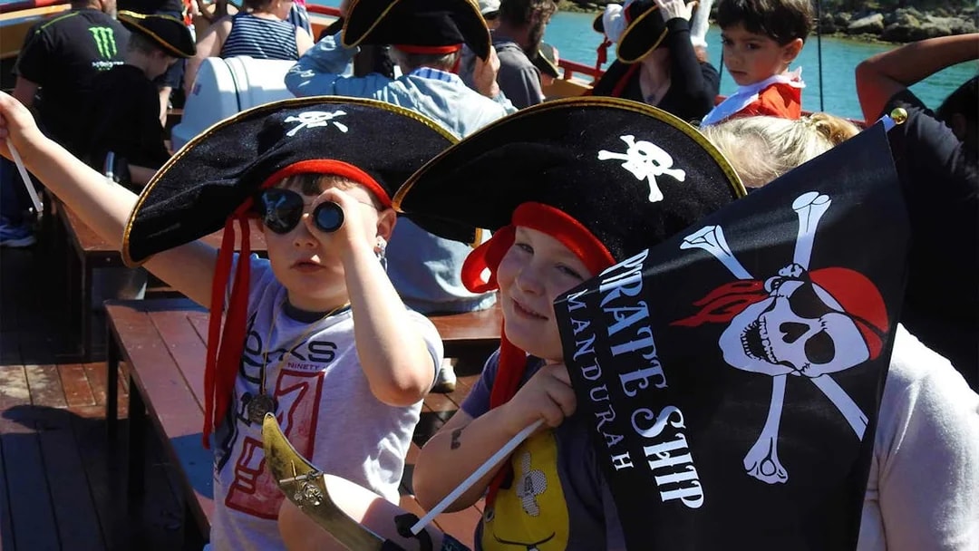 Children dressed as pirates on the Pirate Ship Mandurah holding a flag and telescope.