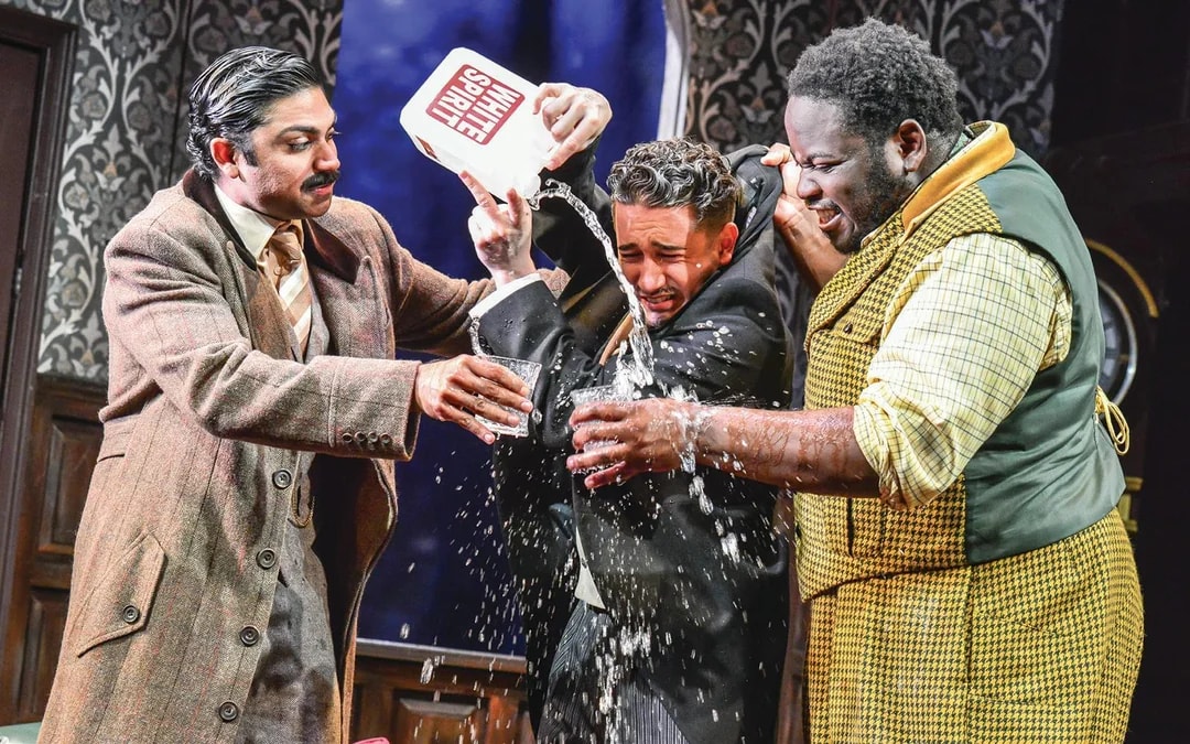 Actors in a comedic scene from "The Play That Goes Wrong" with water being poured.