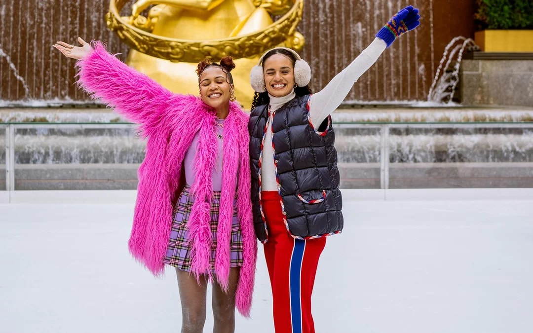 Two people ice skating at Rockefeller Center with Prometheus statue in the background.