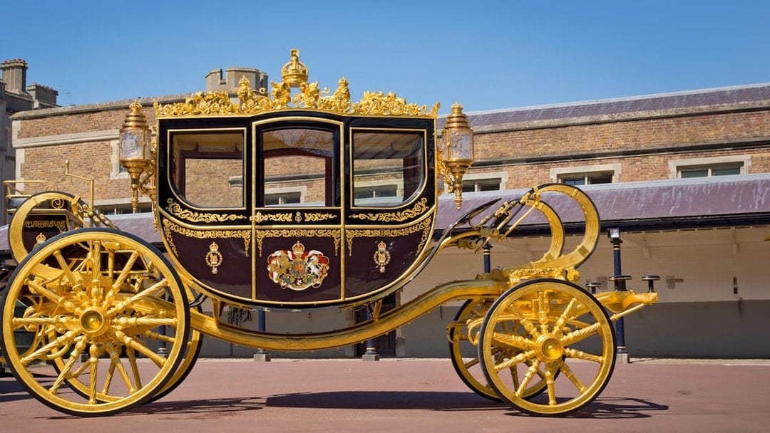 Diamond Jubilee State Coach with ornate gold detailing in front of a historic building.