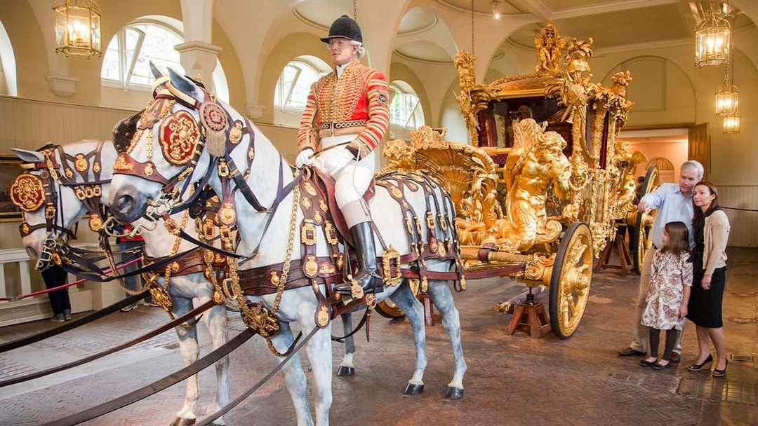 Royal carriage with ornate gold details and tourists observing at Buckingham Palace.
