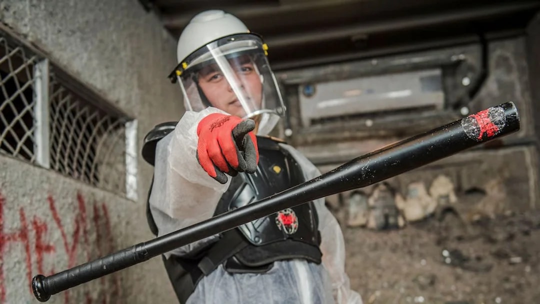 Visitor in protective gear holding a bat in a smash room.