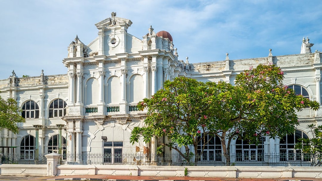 Historic facade of Penang State Museum and Art Gallery, Malaysia, with arched windows and lush greenery.