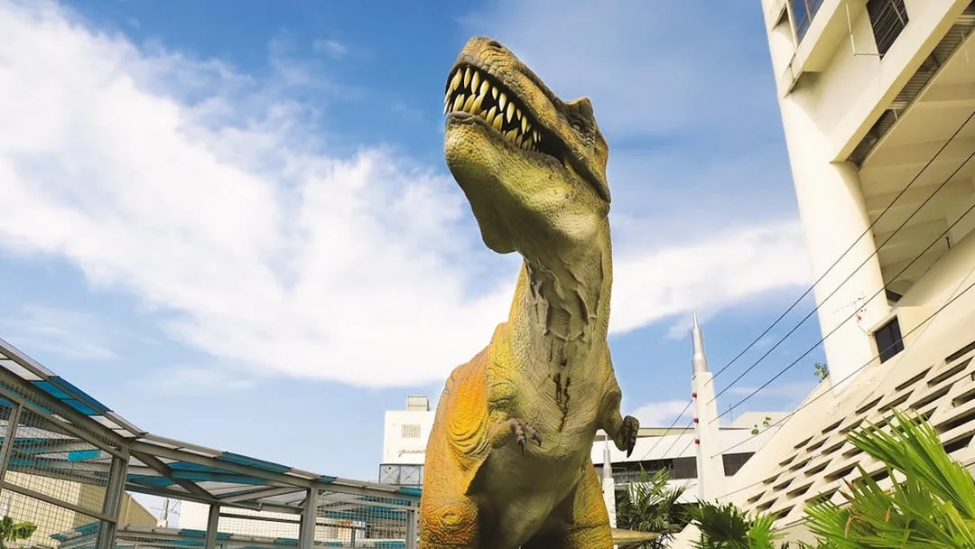 Dinosaur statue at Jurassic Research Centre with buildings in the background.