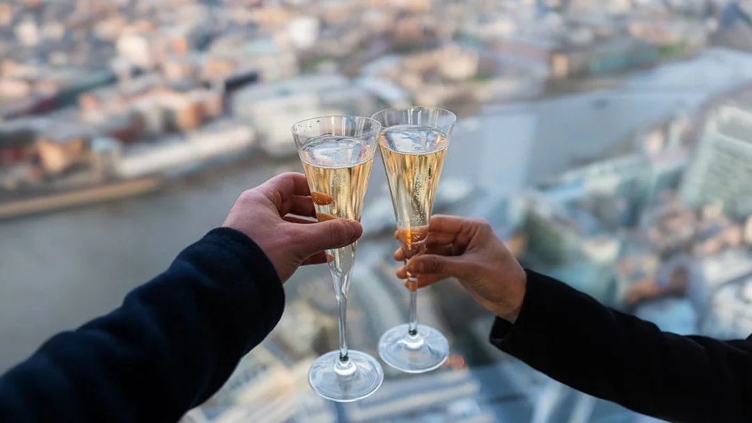 Toasting with champagne at the top of the Shard, London skyline in background.