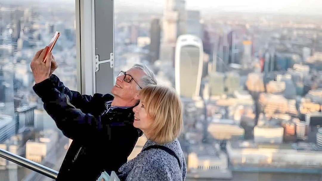Couple taking a selfie at a London skyscraper with cityscape view.