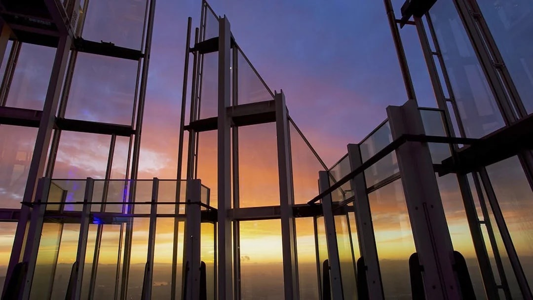 Glass observation deck at sunset with city view.