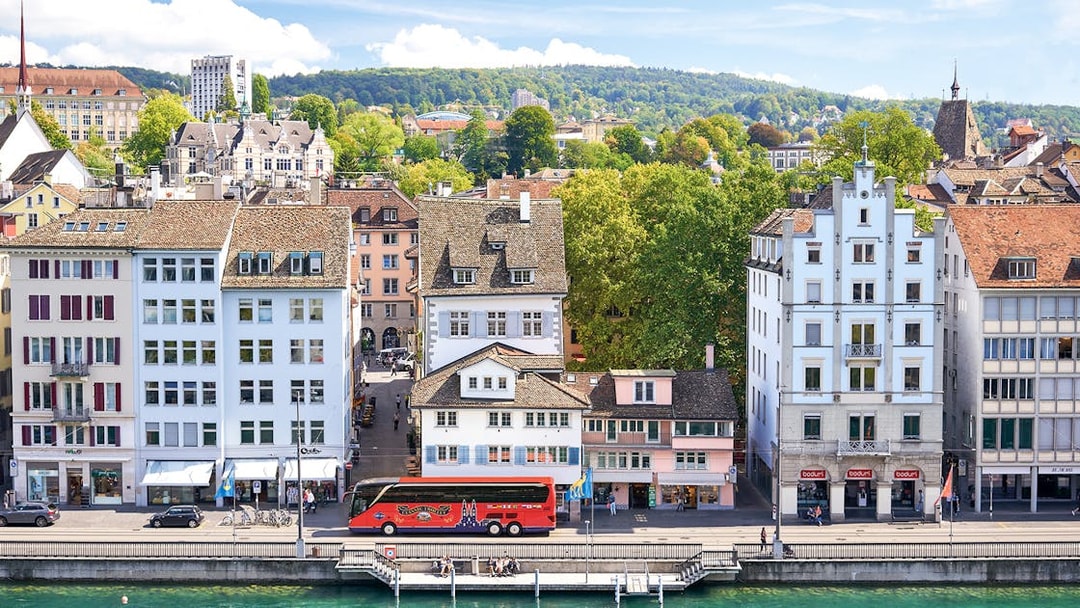 Historic buildings along the Limmat River in Zurich, with a tour bus parked nearby.