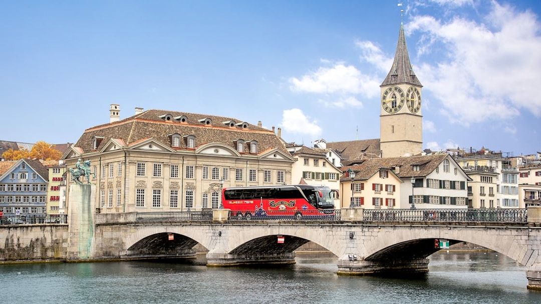 Tour bus crossing Münsterbrücke with St. Peter's Church in Zurich.
