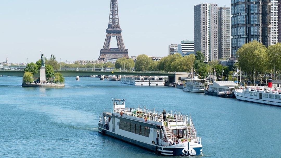 THEO boat cruising on the Seine in Paris with Eiffel Tower and Statue of Liberty replica in view.