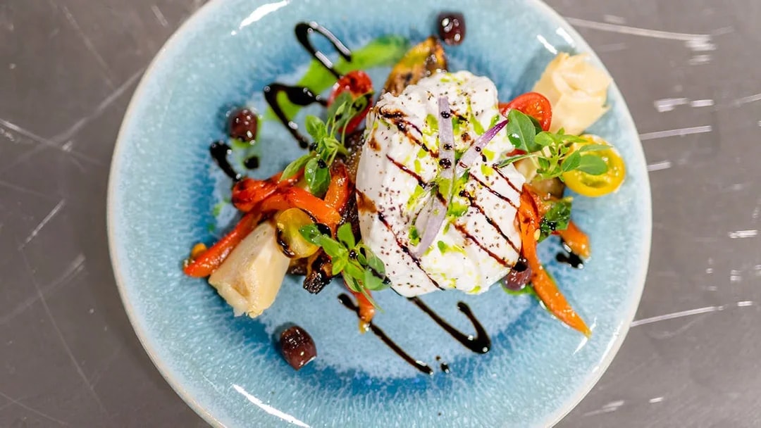Burrata with roasted vegetables and balsamic glaze on a blue plate, served on THEO Boat Brunch cruise in Paris.