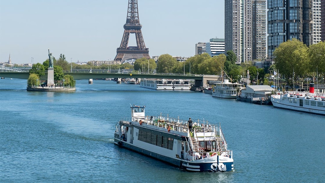 Cruise boat on the Seine River with Eiffel Tower and Paris skyline in the background.