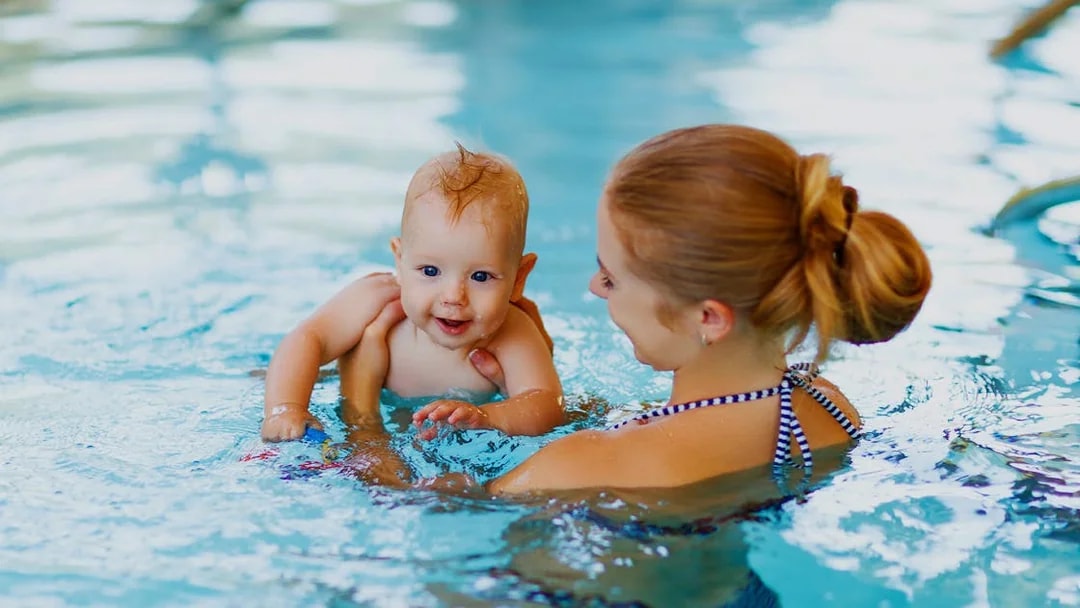 Baby swimming with adult in a pool.