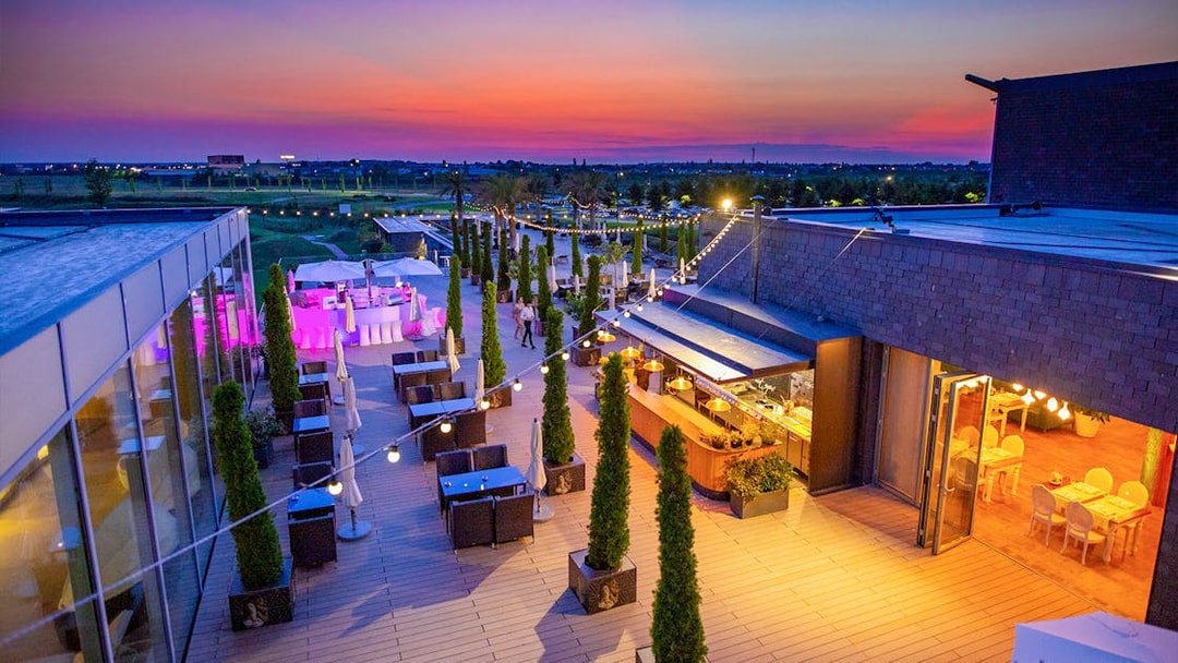 Rooftop terrace at Therme Bucuresti during sunset with dining area and string lights.