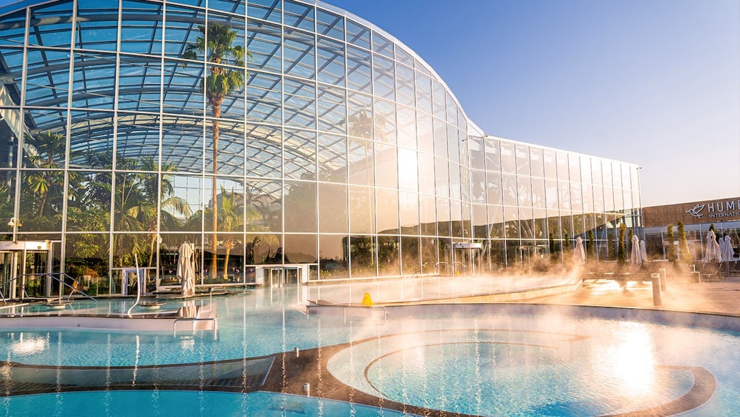 Therme Bucuresti exterior with glass facade and outdoor pool in sunlight.