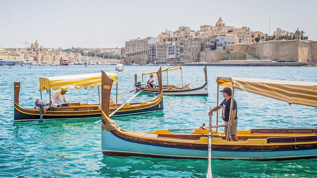 Traditional boats on the water with a view of the Three Fortified Cities in Malta.