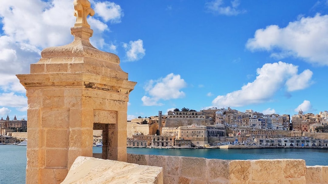 Fortified city view with stone watchtower and harbor, Malta.