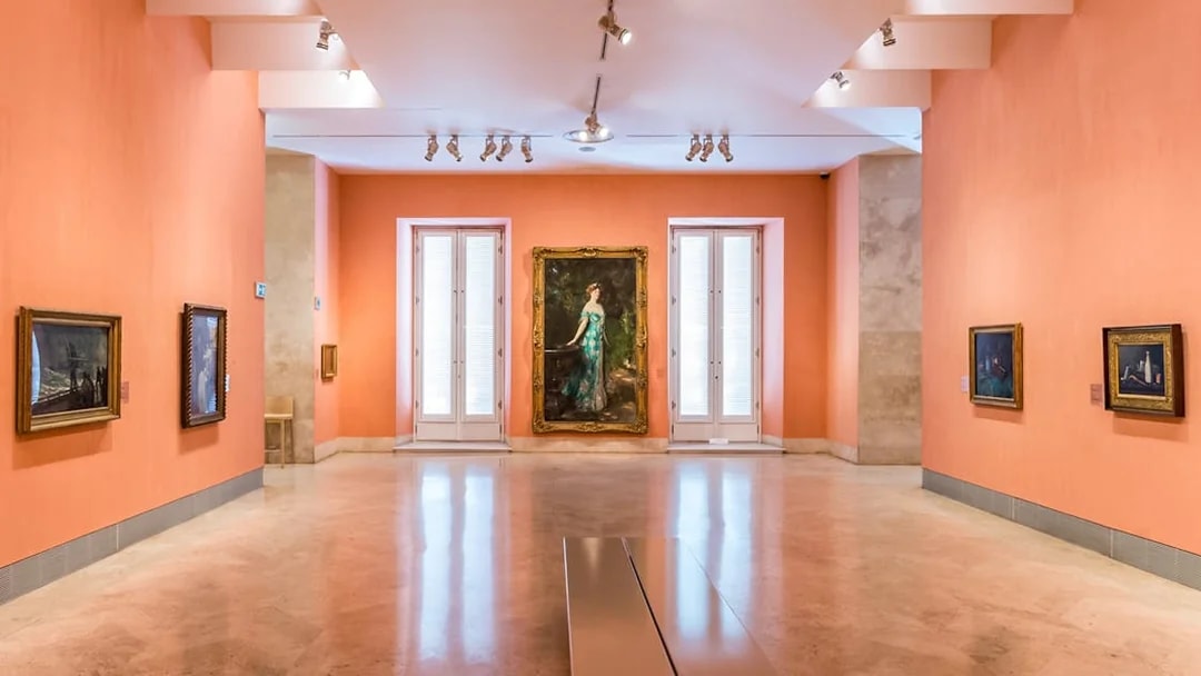 Thyssen Museum gallery with paintings on orange walls in Madrid, Spain.