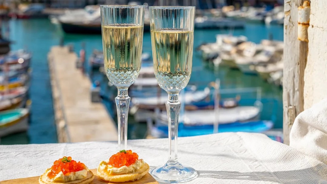 Champagne glasses and appetizers on a table overlooking boats on the Tiber River in Rome.