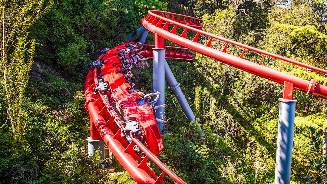 Red roller coaster at Tibidabo Amusement Park, Barcelona, surrounded by trees.